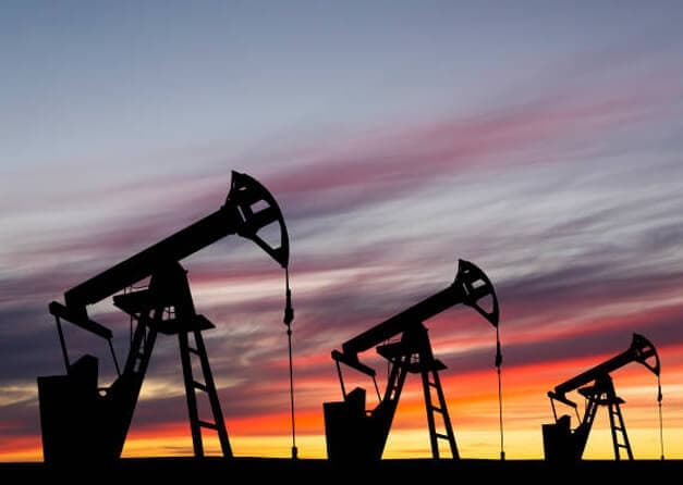 Silhouetted oil pumps against a vibrant sunset sky.