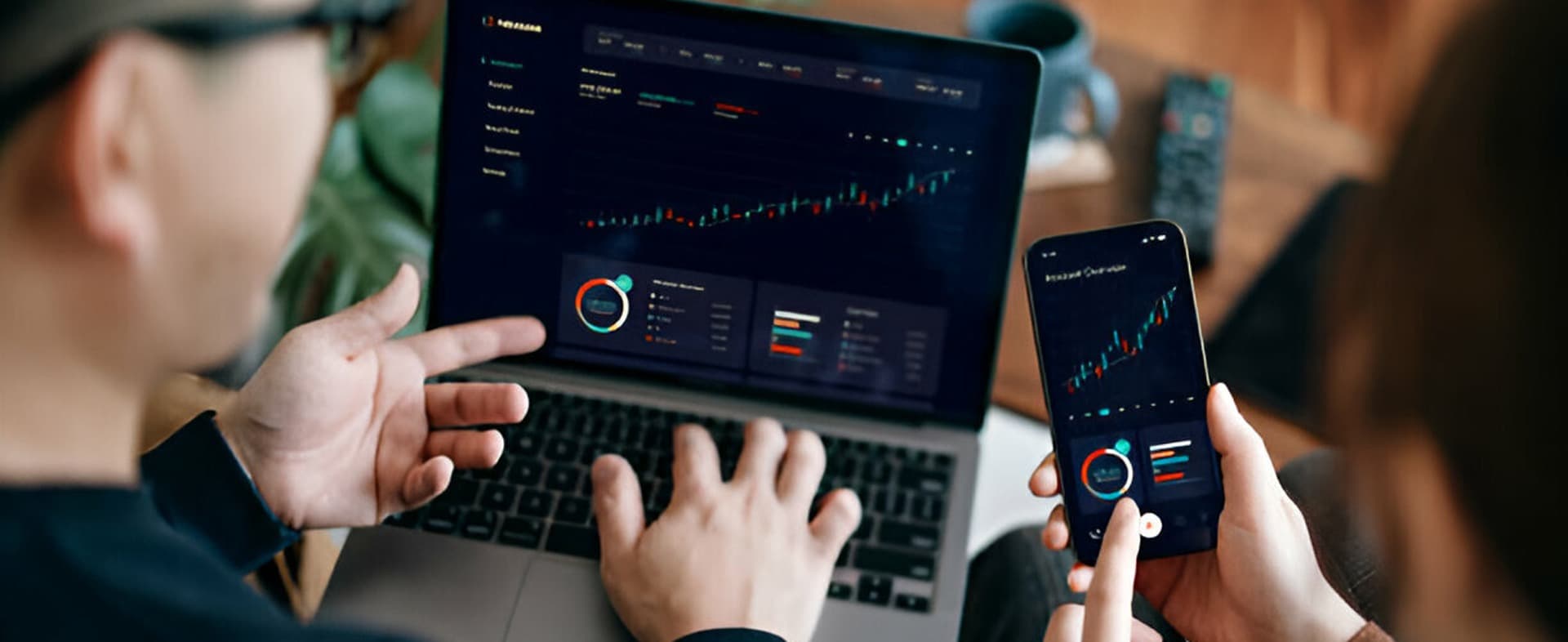 Two people working together, analyzing financial data on a laptop and smartphone.