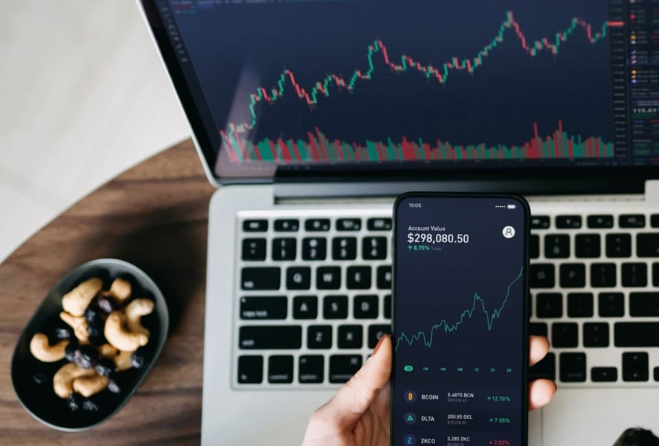 A person analyzing trading charts on a laptop and smartphone.